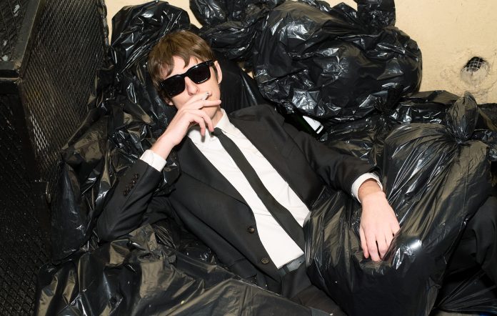 The Dare, pictured in a suit and sunglasses amongst garbage bags, photo by Richard Kern